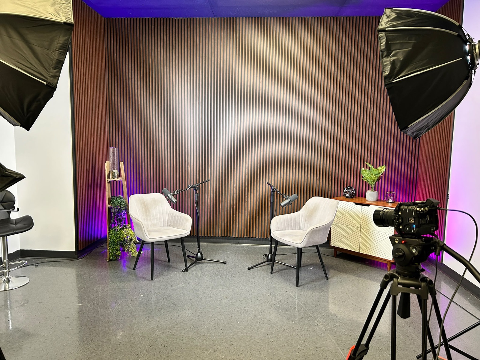 Plateau du studio avec mur de lattes de bois, deux fauteuils, micros et caméra sur pied